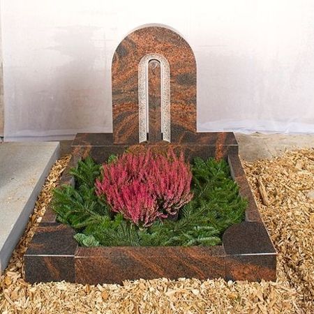 Grabanlage mit rotbraunem Steinbogen und pinker Bepflanzung
